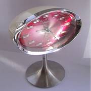 An oval clock with a pink face and reflective silver frame on a pedestal stand.